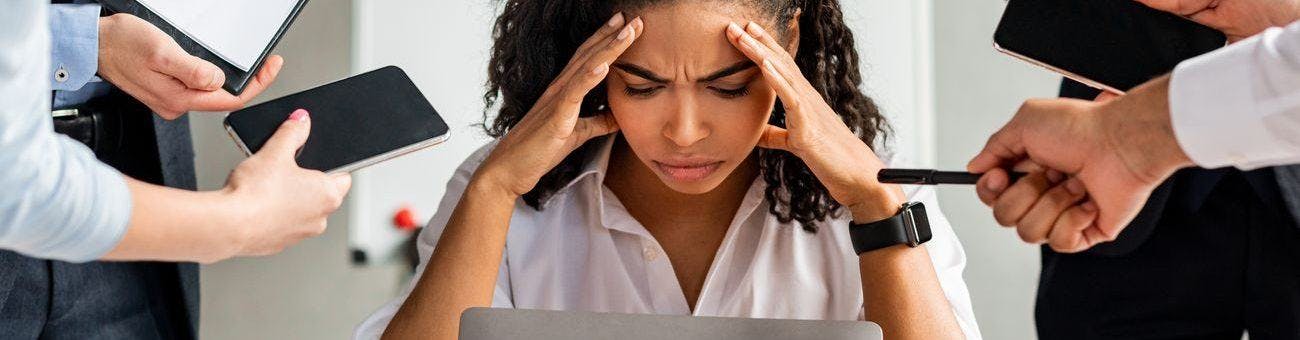 Stressed woman working in front of laptop while co-workers demand her attention.