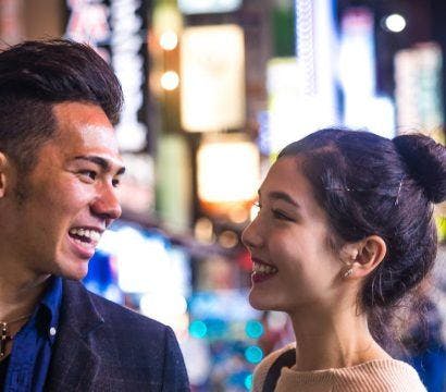 Asian couple smiling against a blurry city background at night.