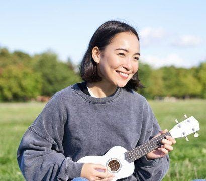 Woman happily sitting on the grass and playing the ukelele.