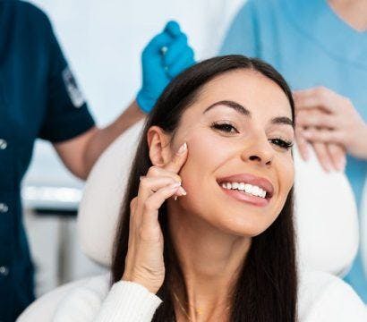 Woman smiling and touching her face with medical technicians in the background.