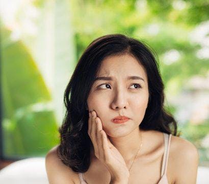 Asian woman looking unhappy, holding her jaw.