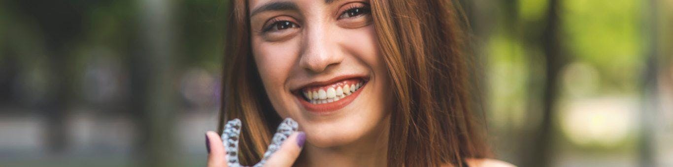 Woman with reddish hair holding clear aligners.