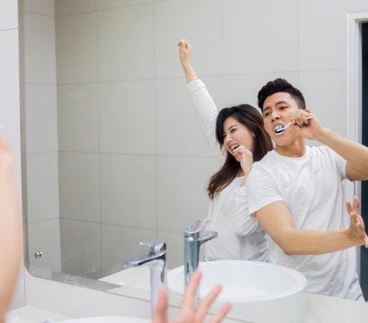 Couple brushing teeth while dancing in front of mirror.