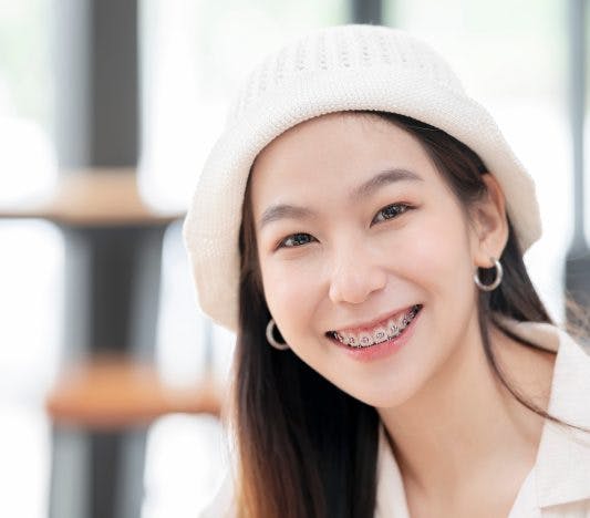 Asian woman with hat and braces smiling.