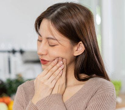 Asian woman holding cheek as if in pain.