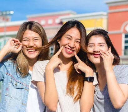 Three female Asian friends laughing and playing with each other’s hair.