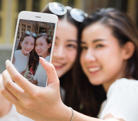 Two women take an outdoor selfie with a mobile phone.