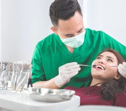 Woman having teeth checked by male dentist in green.