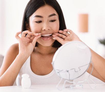 Asian woman happily flossing her teeth in front of a mirror.