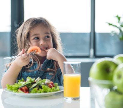 Smiling little girl eating a salad.