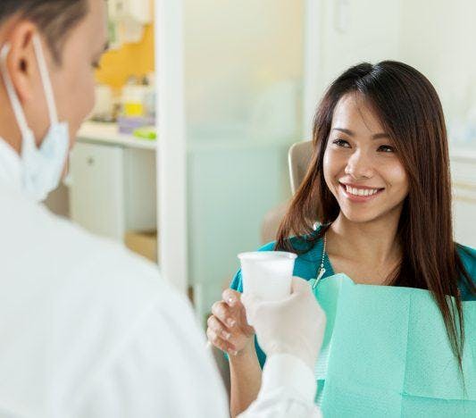 A woman smiling as a dentist hands her a cup.