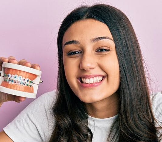 Young woman laughing while holding teeth aligners and teeth model with braces.