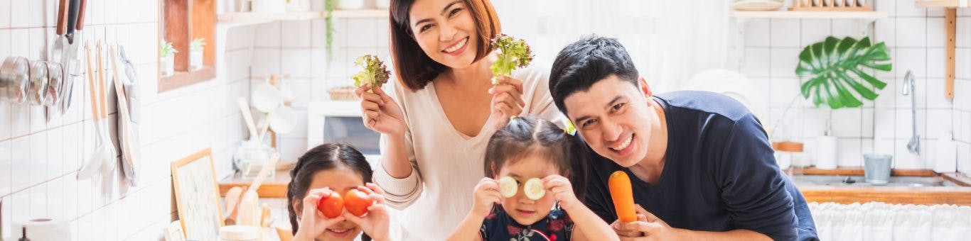 Asian family with daughters happily playing with food and putting slices of vegetables on their eyes.