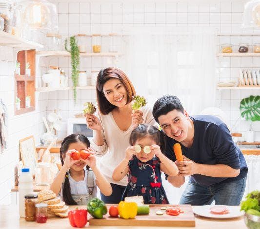 Asian family with daughters happily playing with food and putting slices of vegetables on their eyes.