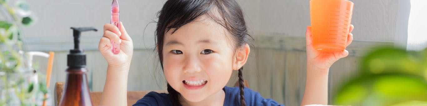 Asian child smiling with a toothbrush and cup.