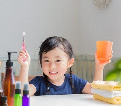 Asian child smiling with a toothbrush and cup.