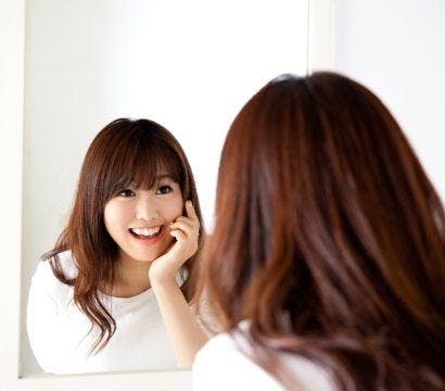 Asian woman with bangs smiling at a mirror.