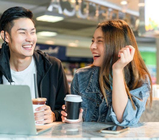 Asian man talking to woman with laptop and coffee.