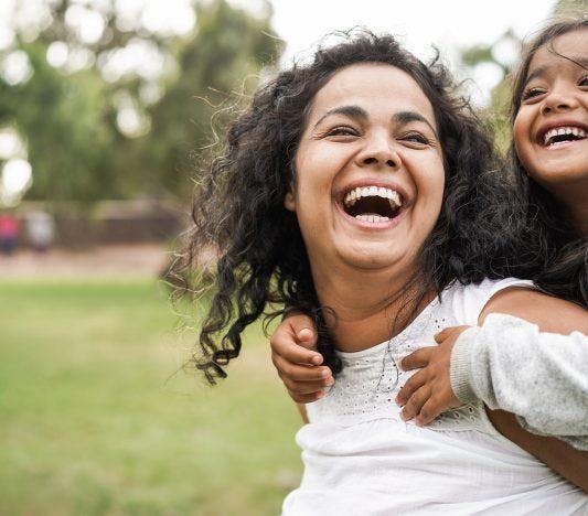 South Asian mom and daughter laughing with grass in background.