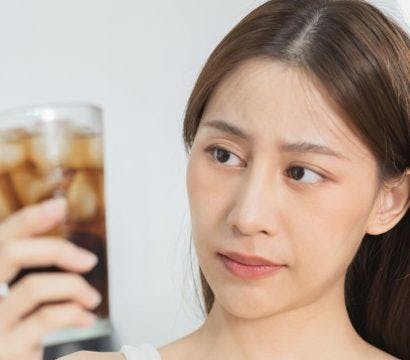 Asian woman looking at a glass of ice-cold soda with concern.