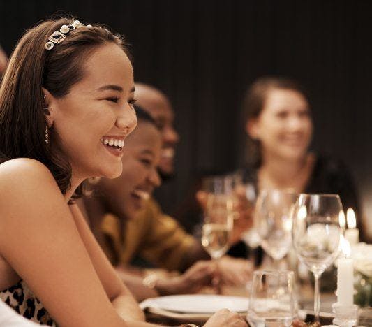 A woman broadly smiling while enjoying dinner with a group.