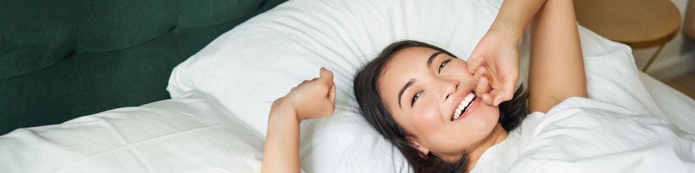 A woman smiling and stretching in bed.