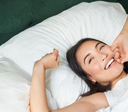 A woman smiling and stretching in bed.