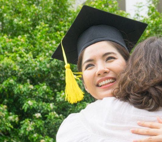 A smiling graduate hugs her mother.