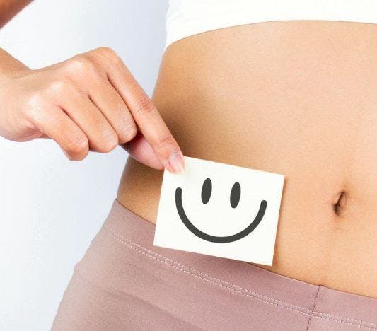 A woman holds up a post-it with a smiley face on it next to her belly.