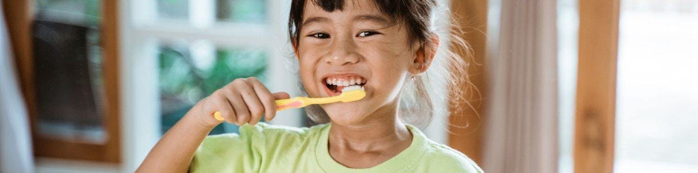 Smiling Asian kid brushing her teeth.