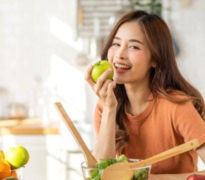 A woman smiling in a kitchen surrounded by fresh and healthy produce.