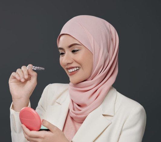 A smiling woman holding her invisible aligners.