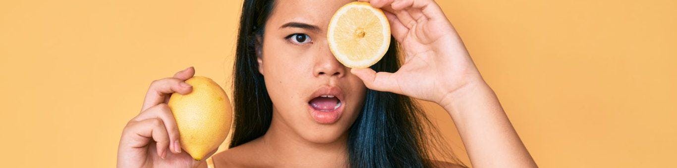 An Asian woman looking surprised while holding lemons.