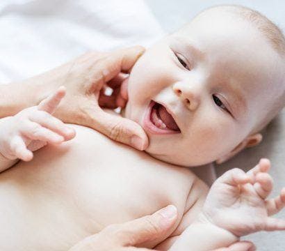 A cheerful baby looking up at their caregiver checking their baby teeth.