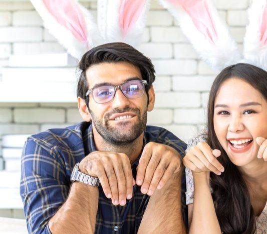 A man and a woman wearing rabbit ears and doing bunny poses.