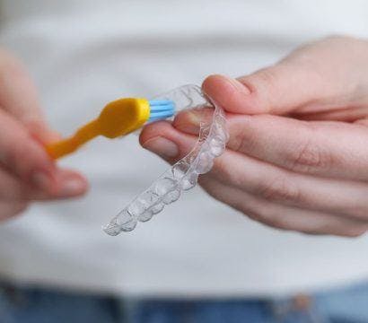 A woman brushing her clear aligners with a toothbrush.