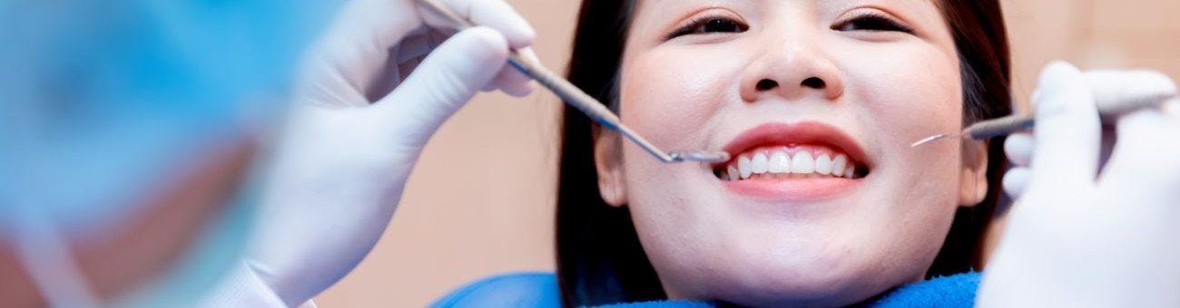 A woman smiling while a dentist checks her teeth.