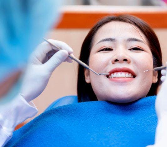 A woman smiling while a dentist checks her teeth.