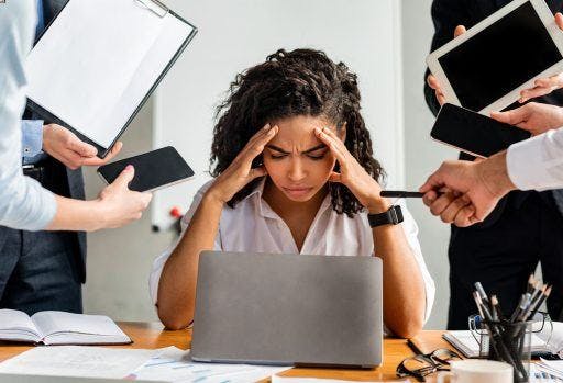 Stressed woman working in front of laptop while co-workers demand her attention.