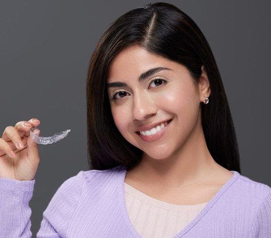 A woman smiling while holding her clear aligner tray.
