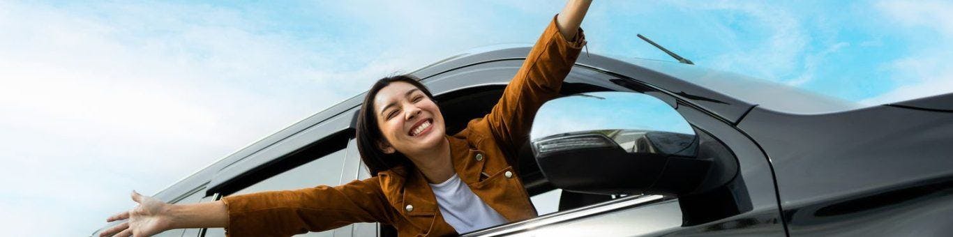 A woman happily extending her head and arms out of a car window.