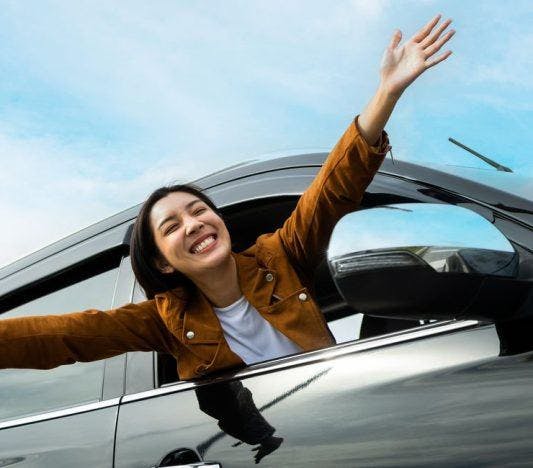 A woman happily extending her head and arms out of a car window.