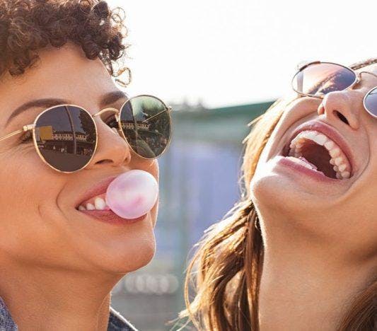 Two women smiling and hanging out; one of them is blowing bubble gum.