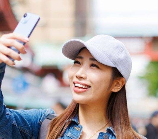 A woman in a cap smiling while taking a selfie.
