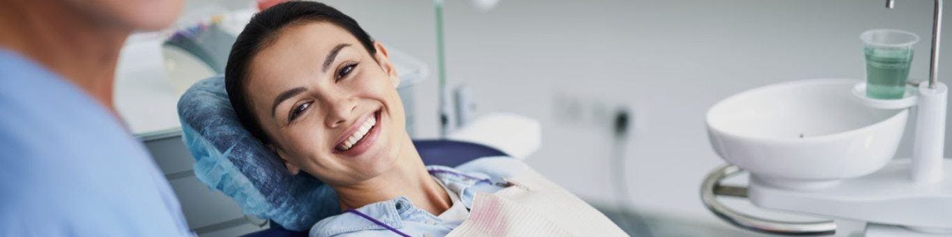 Smiling young woman sitting in a dentist’s chair with a blurred image of a dentist.