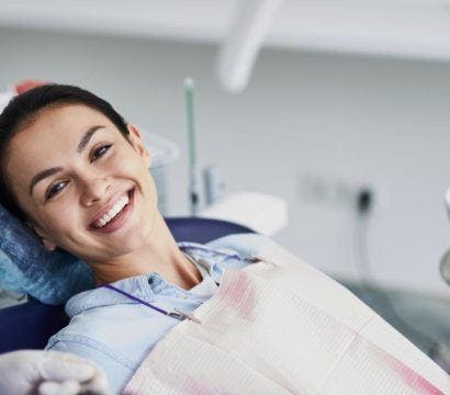 Smiling young woman sitting in a dentist’s chair with a blurred image of a dentist.