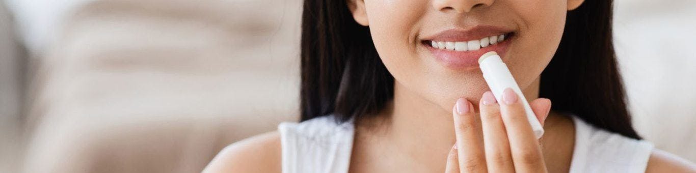 A woman smiling while applying lip balm.