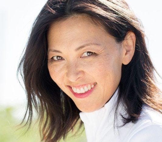 Middle-aged Asian woman in white smiling outdoors.
