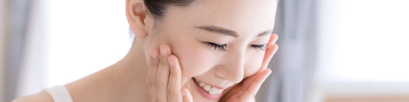 Asian woman smiling and putting her hands on her face in a bright room.