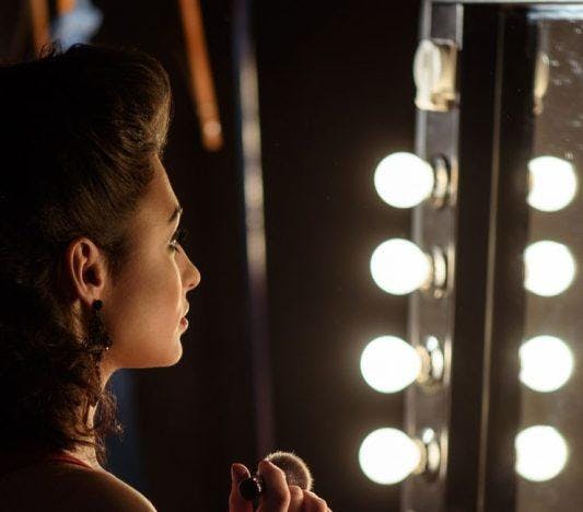 Side view of woman looking into a mirror with lightbulbs.